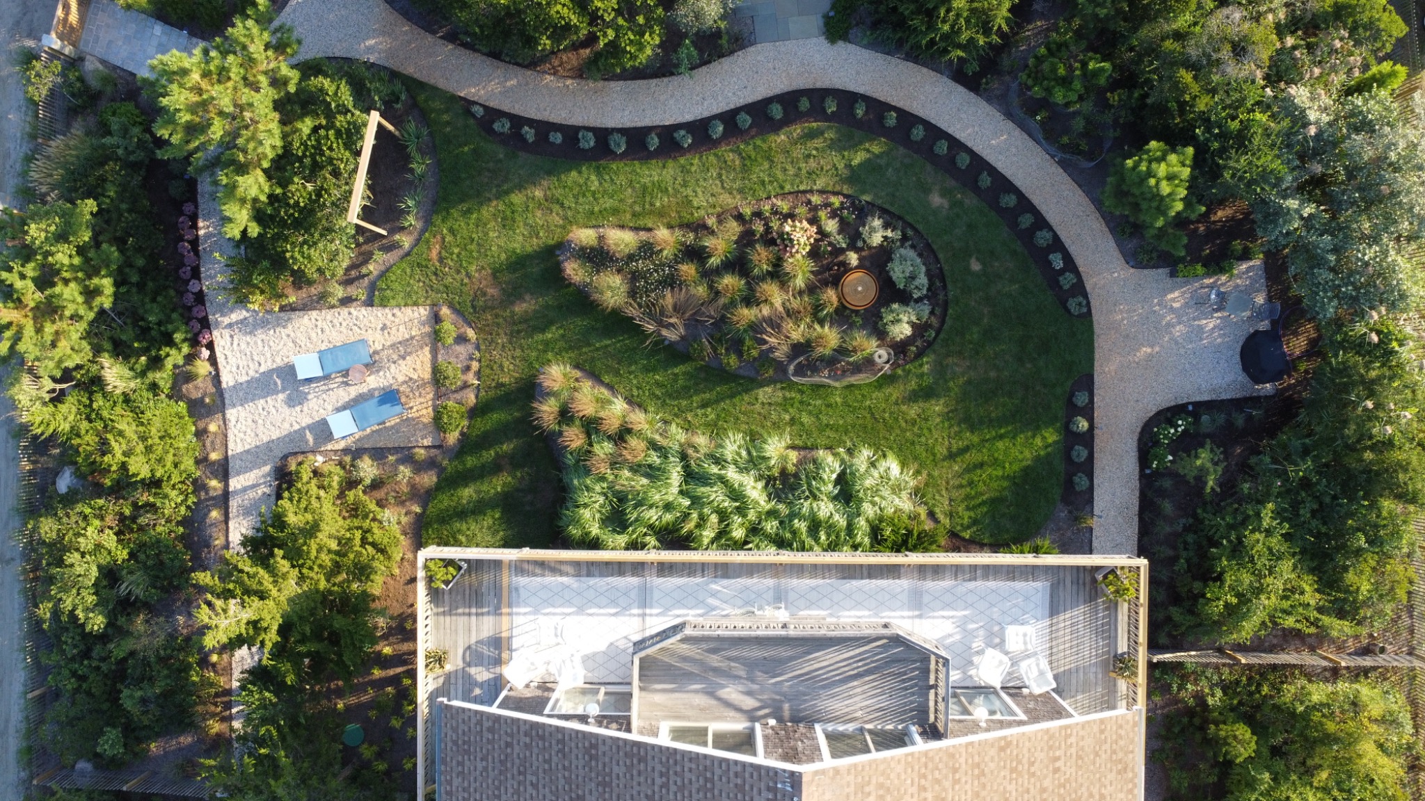 An overhead view of the deck, curved gravel paths, garden fountain, lawn, and blue loungers.